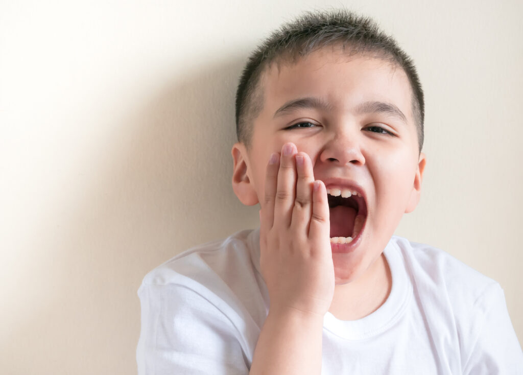 A photograph of a child holding their face due to toothache, illustrating the impact of cavities in baby teeth.